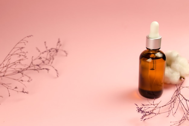 Bottles of cosmetic oil with dried herbs on pink background. 