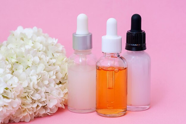 Bottles of different serums on a pink background Facial concept