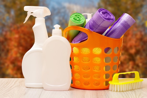 Bottles of dishwashing liquid basket with garbage bags and brush on wooden desk