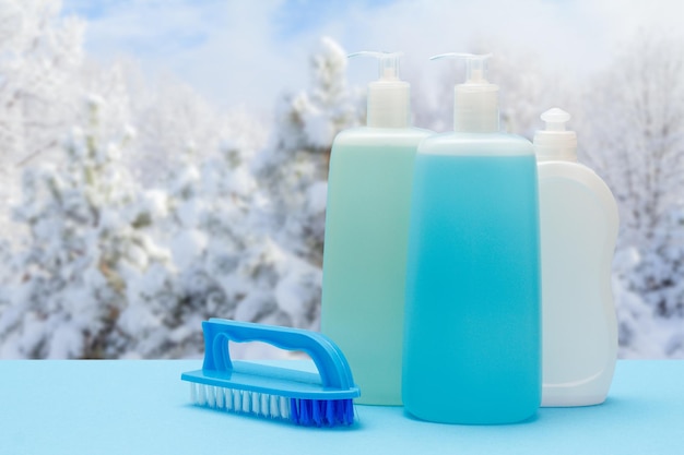 Bottles of dishwashing liquid and brush with winter on background