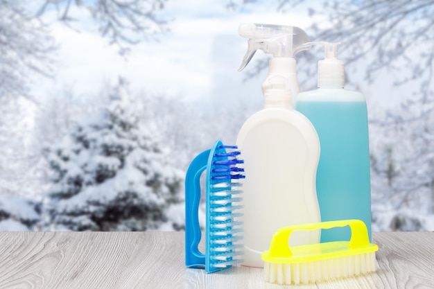 Bottles of dishwashing liquid and brushes with winter on background