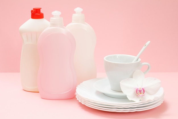 Bottles of dishwashing liquid white plates a saucer a cup on the pink background Washing concept