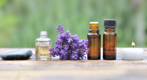 Bottles of essential oil and lavender flowers in line on a table and on green background