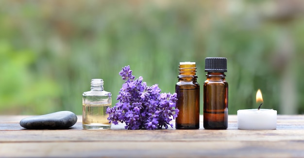 Bottles of essential oil with lavender flower arranged on a wooden table in garden with candle