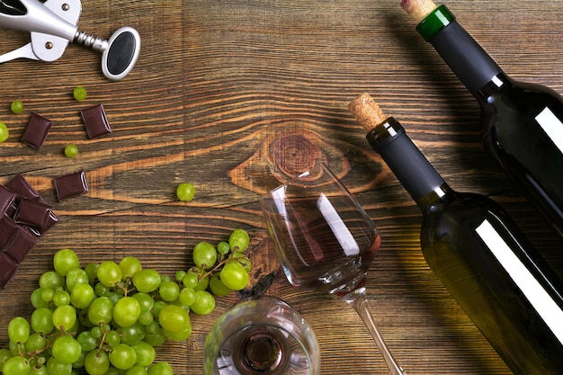 Bottles and glasses of wine chocolate and ripe grapes on wooden background