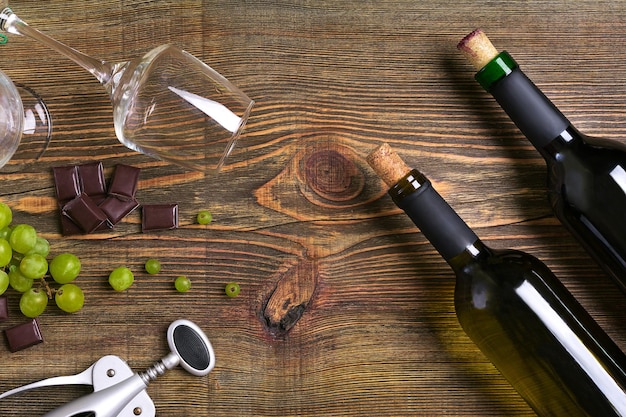 Bottles and glasses of wine chocolate and ripe grapes on wooden background