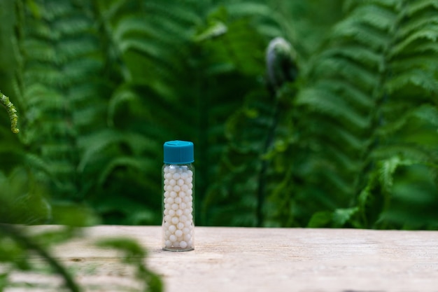 Bottles of homeopathic globules on green fern background. Homeopathy medicine.