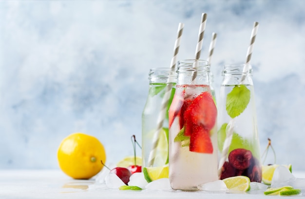 Bottles lemonade refreshing summer lemonade with lime, strawberry, cherry, cucumber and ice on a gray concrete surface. 