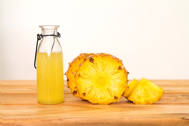 Bottles of pineapple juice with a sliced pineapple fruit on wooden table 