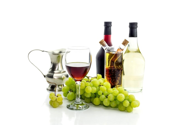 Bottles of wine pitcher glassful and ripe white grapes on a white background closeup