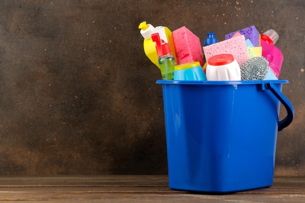 Bottles with cleansers and detergents in a blue bucket on a brown background. cleaning. cleaning products. space for text