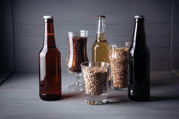 Bottles with craft beer and beer glasses with barley malt on a grey wooden background Ale or lager from pilsner malt homemade homebrewed beer