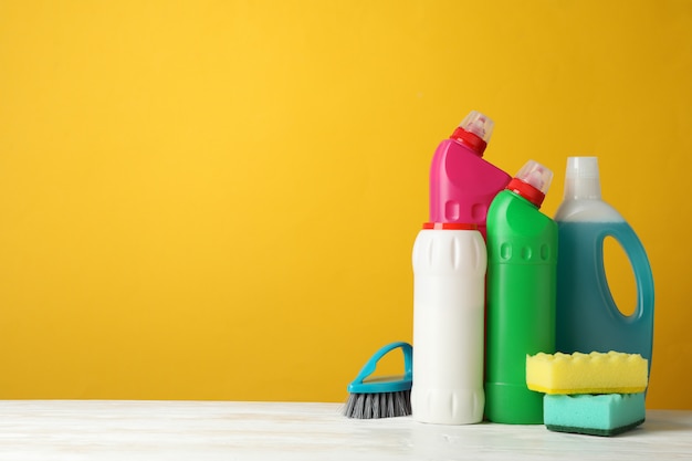 Bottles with detergent and cleaning supplies on yellow background, space for text