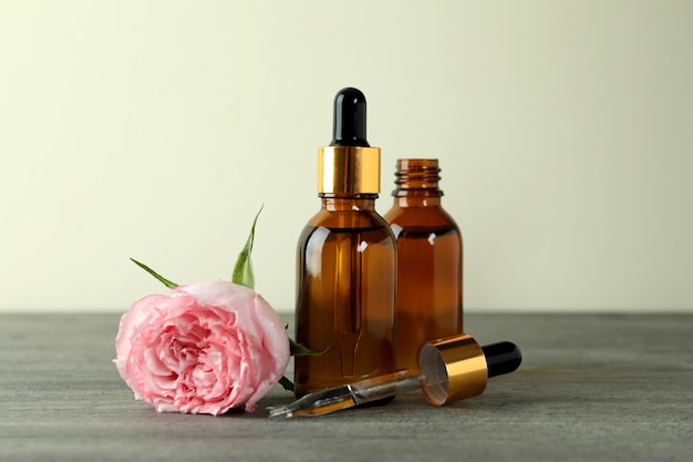 Bottles with rose essential oil on gray textured table