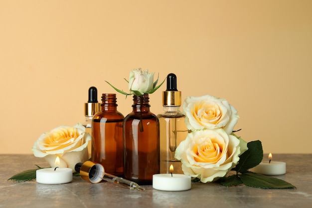 Bottles with rose essential oil, roses and candles against beige