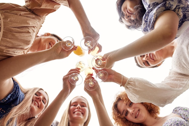 Bottom up view of young charming bride in a white dress and bridesmaids standing in a circle and clinking champagne glasses Beautiful smiling ladies on a wedding party Cheerful bachelorette party