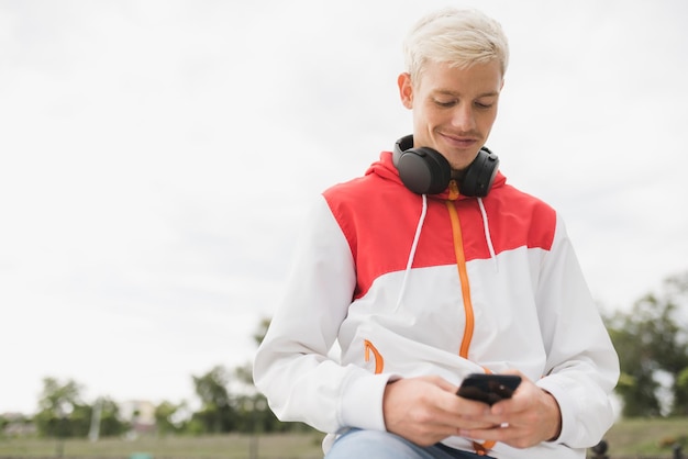 Bottom view of Caucasian man athlete relax after workout outdoor messaging via social networks at smart phone and using headphones for listening to music Healthy lifestyle and people concept