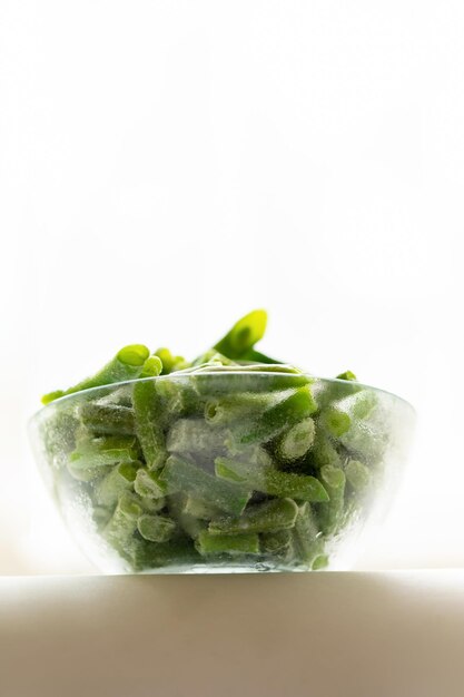 Bottom view to glass bowl with frozen green beans on white Healthy organic food Copy space