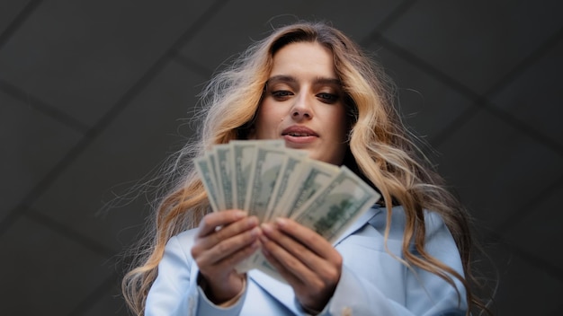 Bottom view successful rich girl business woman buyer holding banknotes dollars in hands counting money salary credit finance thinking holds chin with hand thoughtfully thinks about investment profit