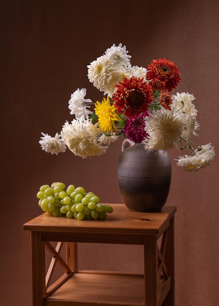 a bouquet of asters on the table next to a large bunch of grapes Still life