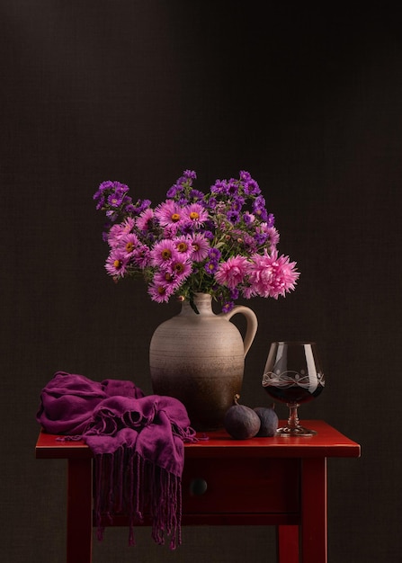 Photo bouquet of autumn flowers glass of red wine on a red wooden table two fresh figs  still life