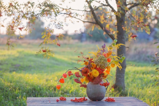 bouquet autumn flowers in rustic jug on wooden table outdoor at sunset