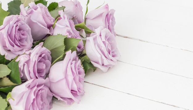 A bouquet of beautiful purple roses on a white wooden background top view with a copy of the space