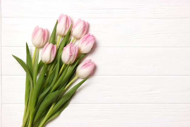 A bouquet of beautiful tulips and a gift on a wooden background top view