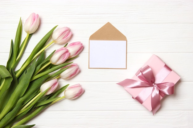 A bouquet of beautiful tulips and a gift on a wooden background top view