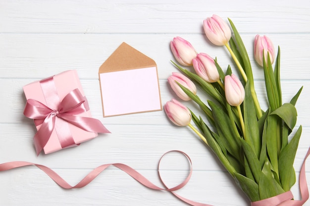 A bouquet of beautiful tulips and a gift on a wooden background top view