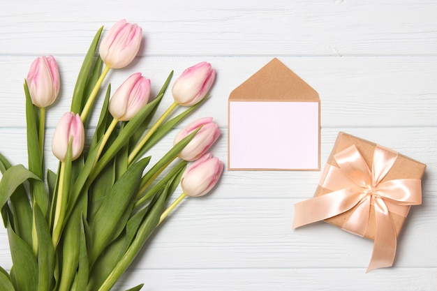 A bouquet of beautiful tulips and a gift on a wooden background top view