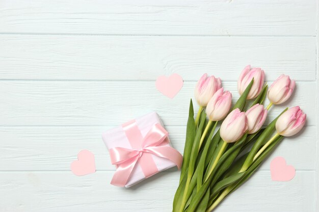 A bouquet of beautiful tulips and a gift on a wooden background top view