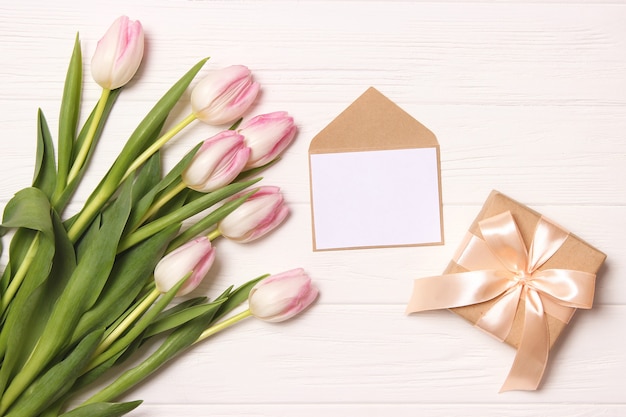 A bouquet of beautiful tulips and a gift on a wooden background top view