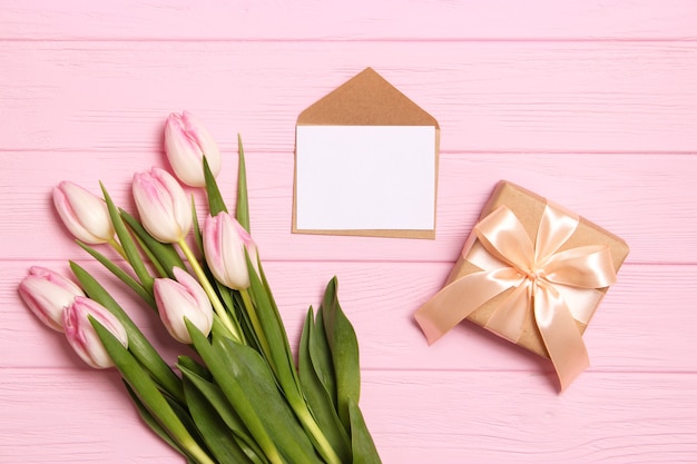 A bouquet of beautiful tulips and a gift on a wooden background top view