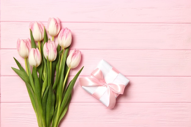 A bouquet of beautiful tulips and a gift on a wooden background top view