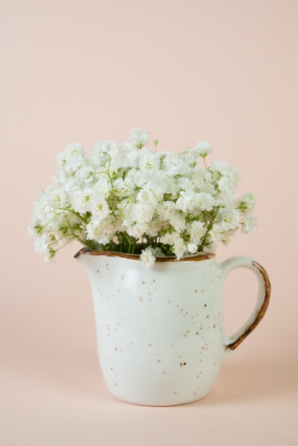 A bouquet of beautiful white spring flowers in a white vase on a pastel beige background.