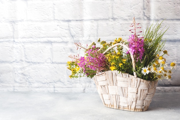 Bouquet of beautiful wildflowers in a basket on a gray background with copy space.