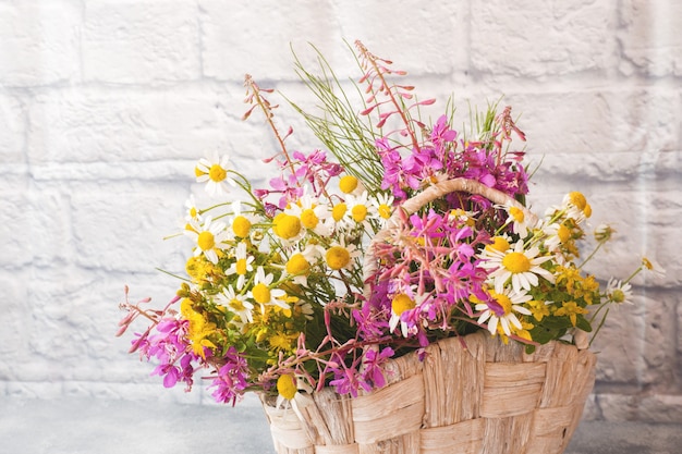 Bouquet of beautiful wildflowers in a basket on a gray surface with copy space.