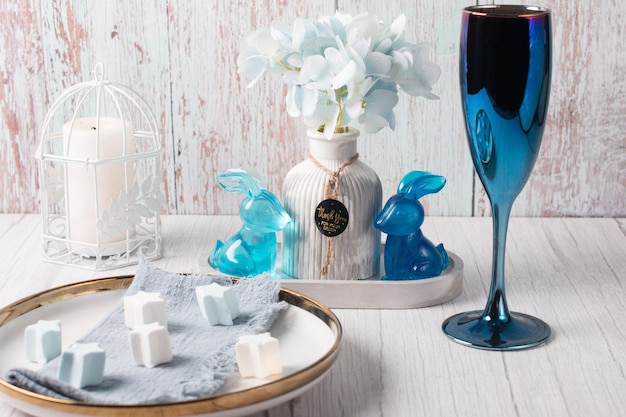 A bouquet of blue carnations with roses Easter blue rabbits with a vase and a candlestick On a wooden rustic background with a blue champagne glass