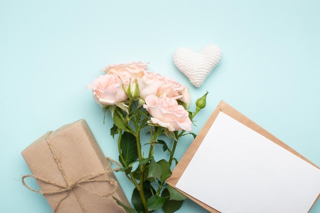 A bouquet of bush roses a gift in kraft paper and a kraft envelope on a light blue background Valentine's Day birthday March 8 Mother's Day Space for copying Flat position top view