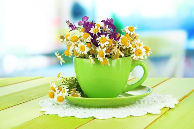 Bouquet of chamomile flowers in cup on bright background