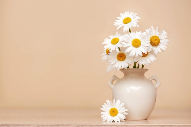 Bouquet of chamomiles in a vase on the table, neutral background. copy space