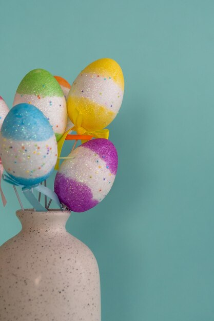 Photo bouquet of colorful easter eggs placed in white vase against blue background