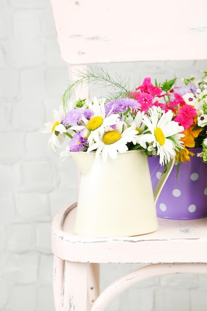 Bouquet of colorful flowers in decorative buckets on chair on light wall background