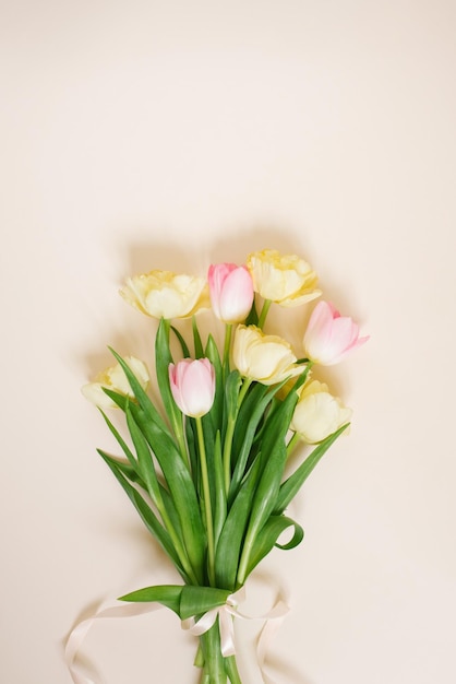 Bouquet of colorful pink and yellow tulip flowers on beige background Spring holidays concept Top view flat lay copyspace