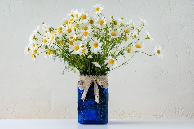 Bouquet of daisies in blue jar on light background