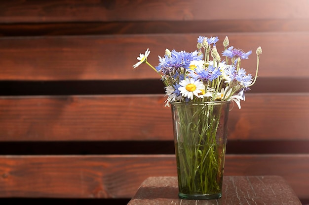 A bouquet of daisies and cornflowers in a glass vase in the sun