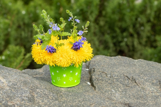 Bouquet of dandelions and blue flowers in a bucket on a stone. Dandelion flowers. Copy space. Place for an inscription. Selective focus.