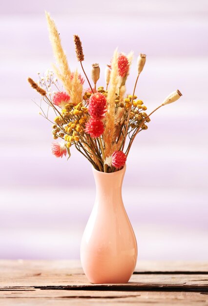 Bouquet of dried flowers in vase on color planks background