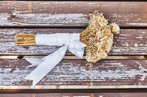 Bouquet of dried roses tied with white ribbon lying on bench at sunset